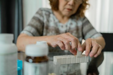 Asian Senior woman  Senior putting medications in a daily pill organizer and closing the lids.