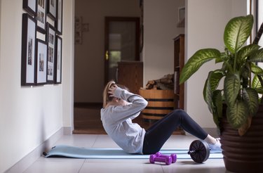 Person in gray sweatshirt and black leggings doing sit-ups in living room