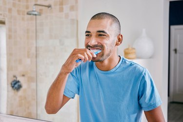 Person in blue shirt brushing their teeth in a bathroom at home.