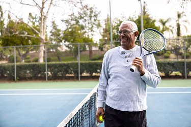 Portrait of an older adult on the tennis court smiling and holding a tennis racquet in one hand