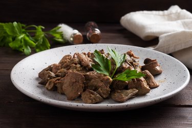 Fried or baked chicken liver with onion and sauce, green parsley leaves on a plate. Meat dish enriched with iron.