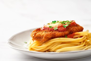 low-angle view of L-lysine-rich chicken Parmesan and spaghetti on a white plate
