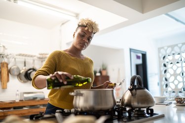 Young woman preparing food at home using avocado oil