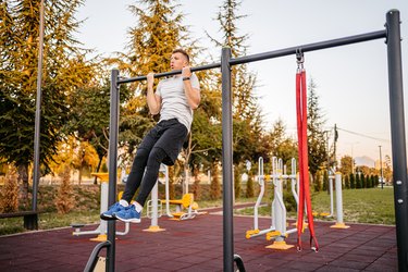 Person wearing a white T-shirt and black pants doing chin-ups vs. pull-ups in the park