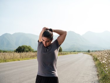 Person wearing gray T-shirt and black pants stretching triceps outside with mountains in background