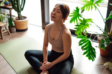 Person wearing athletic clothes sitting on a light green yoga mat practicing meditation at home, as a way to build resilience