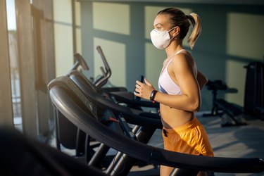 woman with face mask running on treadmill in health club.