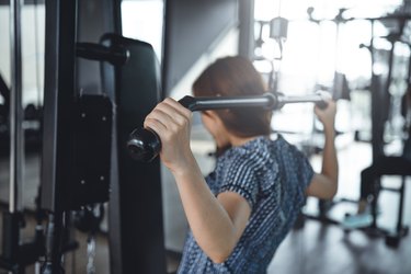 Close up woman using lat pulldown machine in gym fitness.