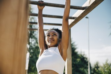 Athlete performing a dead hang on monkey bar in park