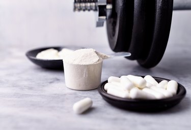 Scoop of creatine powder with capsules and a dumbbell on marble