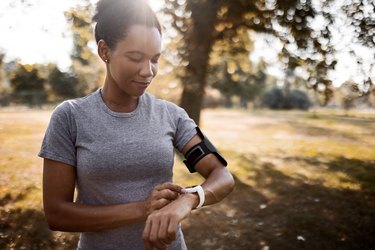 black woman outside, looking at running watch to track her running split times