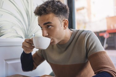 a person wearing a colorblock sweater drinking coffee out of a white mug in a cafe