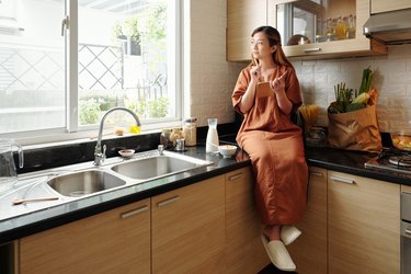 woman sitting on her kitchen counter and writing in a gratitude journal, as a way to practice body acceptance