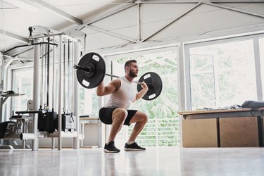 Young man doing barbell back squats