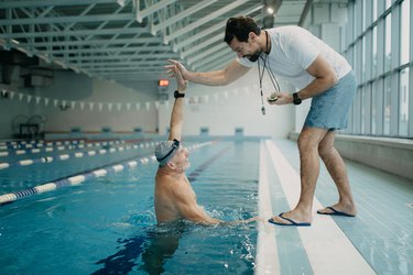 Swim coach encouraging swimmer in indoor pool after swimming 100 meters.