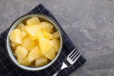 Healthy canned pineapple in bowl on grey table, flat lay. Space for text