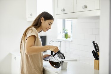 Young woman pouring coffee in cup at home