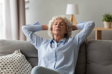 an older woman sitting on her couch at home and doing a deep breathing exercise, as a natural remedy for fibroids