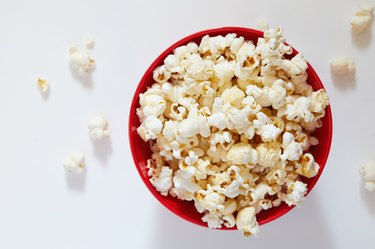 Overhead view of a red bowl of popped popcorn on white table