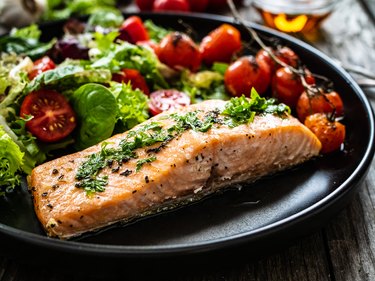 Fried salmon or trout steak, roast potatoes and fresh vegetables on wooden background