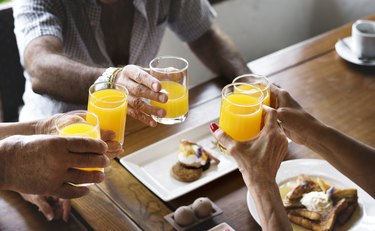 people clinking orange juice glass together at breakfast