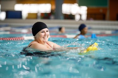 Adult wearing black swim cap, holding water weights while doing water aerobics