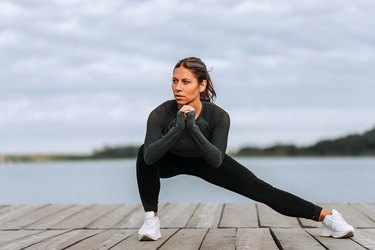 一个健康的女人在河边做侧弓步的前视图。