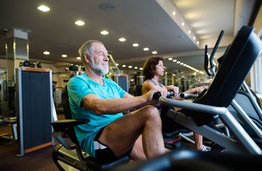 an older couple rides a recumbent bike in a gym