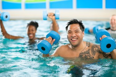 smiling person with short hair and a large shoulder tattoo doing water aerobics in the pool with weights
