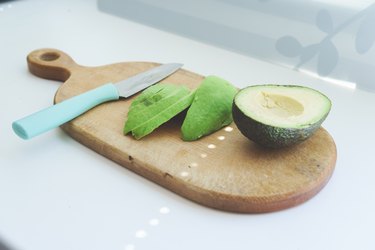 Half an avocado and avocado slices on a wooden cutting board on a white table is a type of foods that is the best source of calories