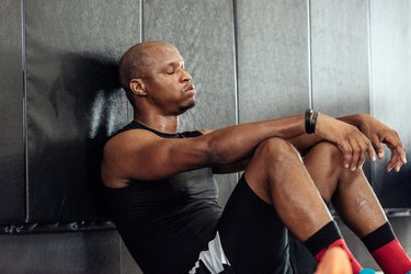 Exhausted man needing a rest day, sitting down with eyes closed and taking a break from exercising