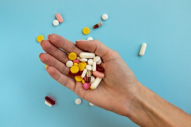 Woman holding in hand different medical pill on light blue background.