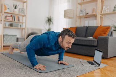 Man doing push-ups in living room during streaming workout on computer