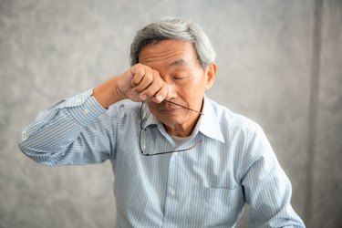 older adult holding eyeglasses and rubbing their eyes wearing light blue button down shirt as example of sudden extreme sleepiness with age