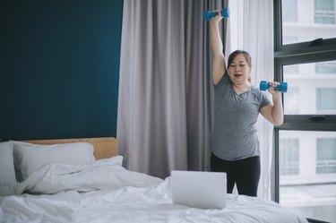woman doing an arm workout with dumbbells at home in her bedroom to get rid of the fattest arms and chubby arms