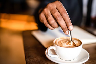 Man's hand mixing coffee and collagen with a spoon