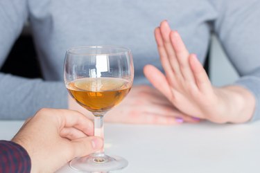 close view of a woman holding up her hands to refuse a glass of alcohol, as a natural remedy for fibroids