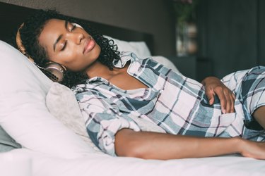 woman wearing headphones and listening to a podcast in bed, as a natural remedy for insomnia