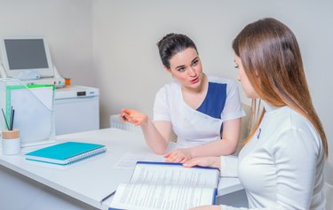 Young female doctor sits at her desk and chats to female patient while showing her test results