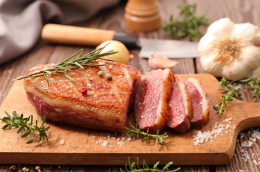 freshly roasted iron-rich duck roast sliced with rosemary and garlic on cutting board