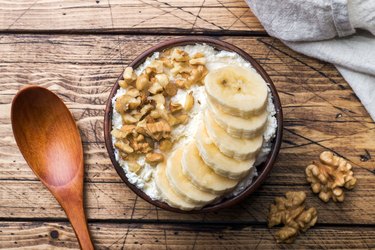 Cottage cheese with banana and walnuts on wooden background.