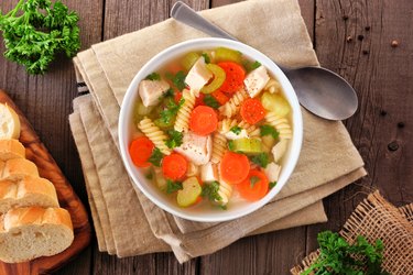 Homemade rotisserie chicken noodle soup with vegetables, overhead table scene on wood