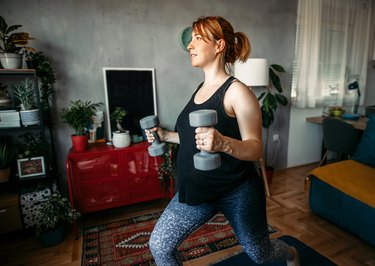 Pregnant woman doing exercises with dumbbells at home - a Royalty