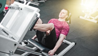 athletic adult wearing a red shirt and black shorts using the seated leg press machine in a gym