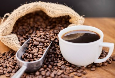 Shot of coffee beans and a cup of black coffee, a food high in phosphoric acid,  on a wooden table