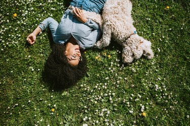 一名女子带着宠物贵宾犬在草地上休息