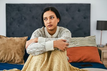 Young person wearing a grey sweater and yellow blanket curled up in bed because they have no energy from the flu