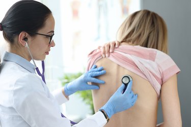 Healthcare provider listening to a patient's lungs and breathing with a stethoscope.