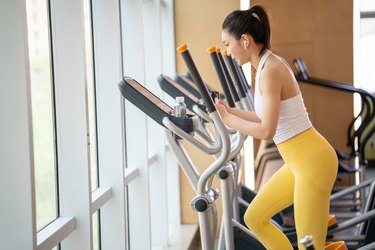 Younger person in yellow leggings using the elliptical at the gym