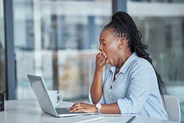 A business person yawning while at work on their laptop.